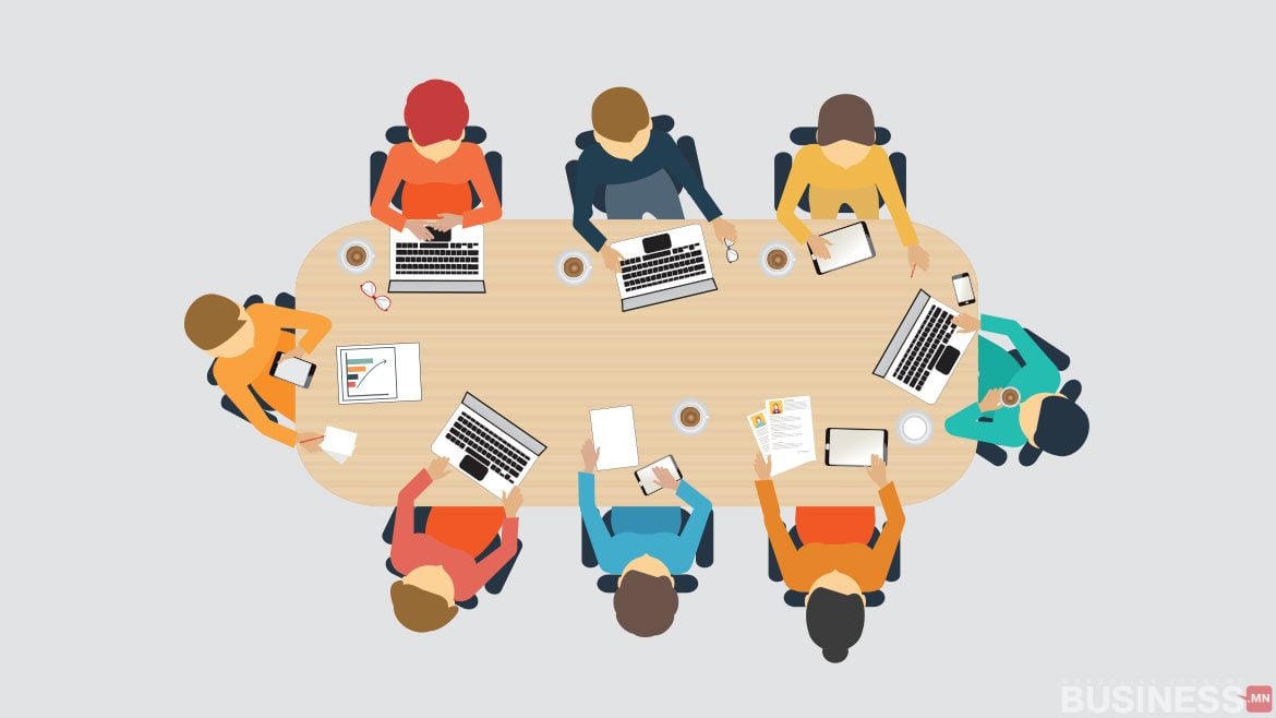 Зууван хэлбэрийн хурлын ширээг тойрон сууж, зөөврийн компьютер, баримт бичиг дээр ажиллаж буй найман бизнес эрхлэгчийн дүрслэл. - Business.MN