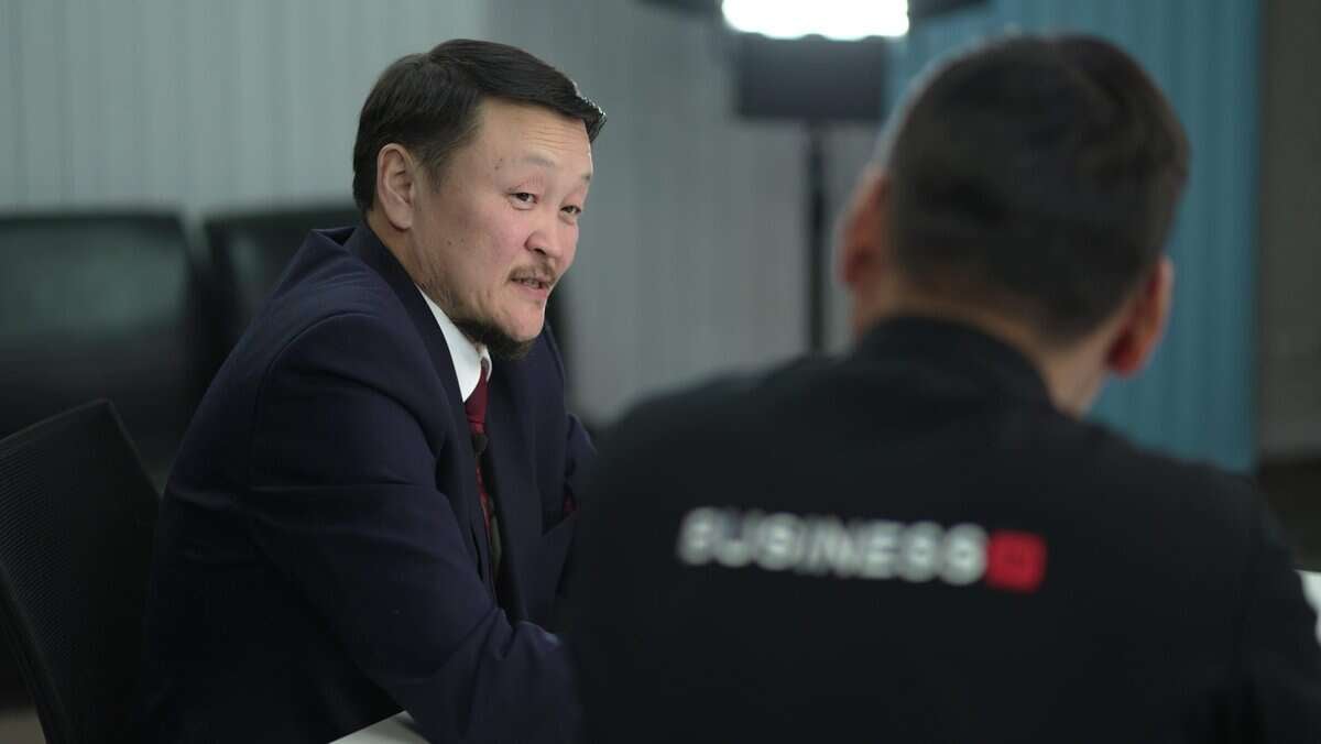 Хоёр эрэгтэй ширээний ард суугаад харилцан яриа өрнүүлж байна. Зүүн талд байгаа эрэгтэй костюм, зангиатай, ар талдаа "БИЗНЕС" гэсэн бичигтэй бараан өнгийн цамц өмссөн нөгөө залуу руу анхааралтай харна. Цаана нь тод гэрэл асч, тэдний бизнесийн хэлэлцүүлэгт урам зориг өгч байна. - Business.MN