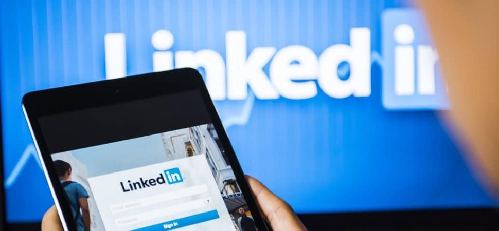 LinkedIn-д нэвтрэх дэлгэцтэй таблет барьсан бизнес эрхлэгч LinkedIn лого бүхий том дэлгэцийн өмнө зогсож, бизнесийн мэргэжилтнүүдтэй холбогдож, компаниа өргөжүүлэхэд бэлэн байна. - Business.MN