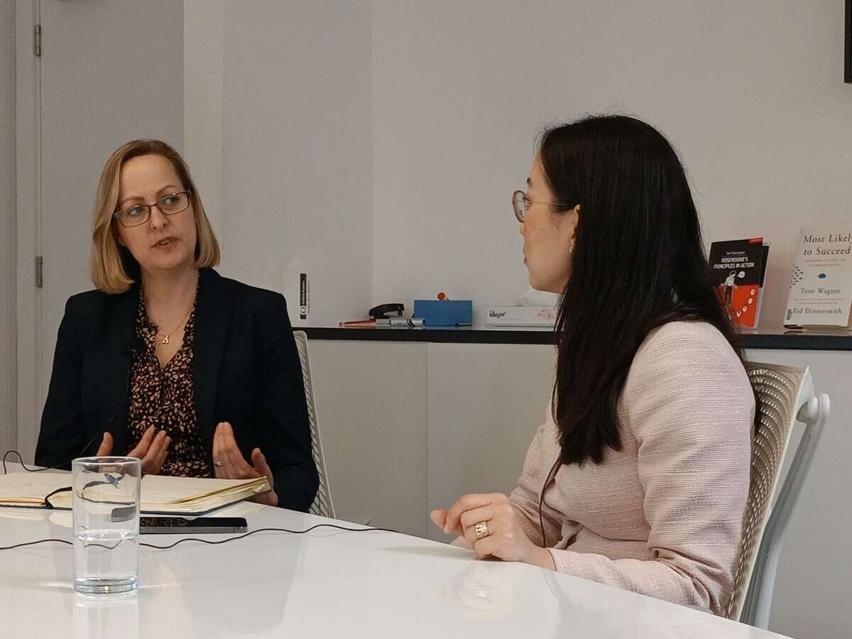 Хоёр эмэгтэй ширээний ард сууж, компанийнхаа талаар ярилцаж байна. Зүүн талд байгаа эмэгтэй бараан пиджак, хээтэй цамц өмссөн гараараа дохиж байна. Баруун талд байгаа эмэгтэй нүдний шил, цайвар өнгийн пиджак өмсөж, анхааралтай сонсож байна. Ширээн дээр нэг аяга ус сууна. - Business.MN