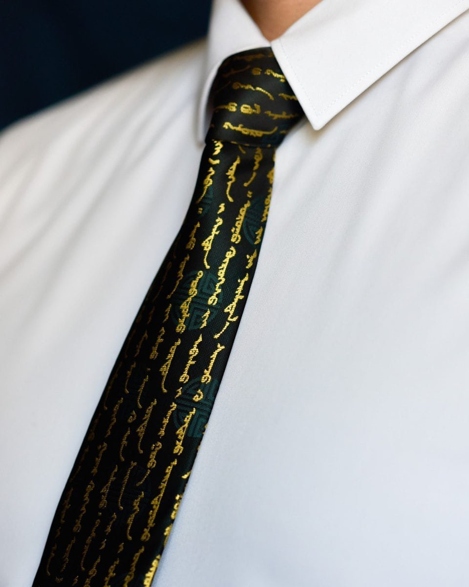 A person wearing a white dress shirt and a black necktie decorated with gold Elvish script from The Lord of the Rings.