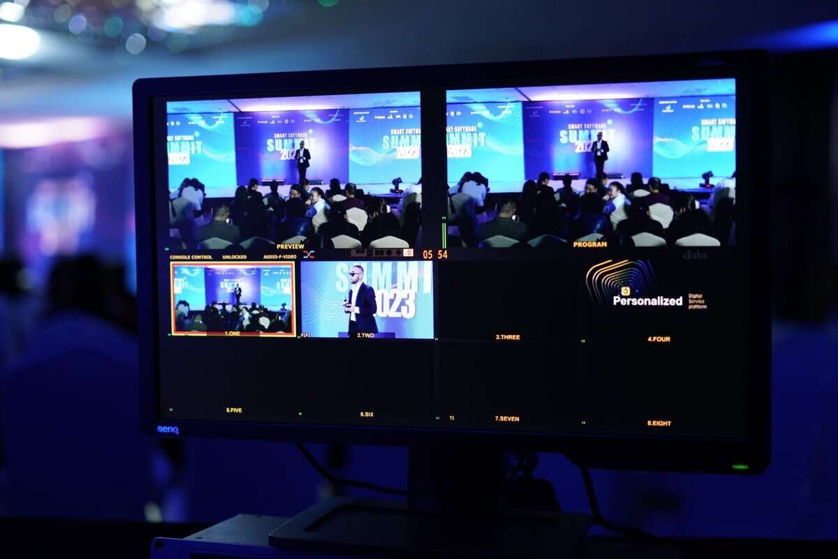 Дэлгэц нь илтгэгч болон үзэгчидтэй хурлын тайзыг хуваасан дэлгэцээр харуулдаг. Дэлгэц нь "Summit 2023" нэртэй арга хэмжээний шууд видео бичлэг болон хөтөлбөрийн дэлгэрэнгүй мэдээллийг харуулдаг. Арын дэвсгэр нь бүдэгхэн гэрэлтэй бөгөөд бизнесийн удирдагчид болон компанийн төлөөлөгчдөд зориулсан бизнес эрхлэгчийн ойлголтыг агуулсан эрч хүчтэй дэлгэцийг онцолж байна.
- Business.MN