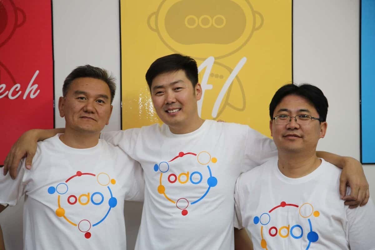 Өнгө өнгийн лого бүхий цагаан подволк өмссөн гурван энтрепренер хамтдаа зогсож, бие биенээ тэврэн, бахархалтайгаар инээмсэглэв. - Business.MN