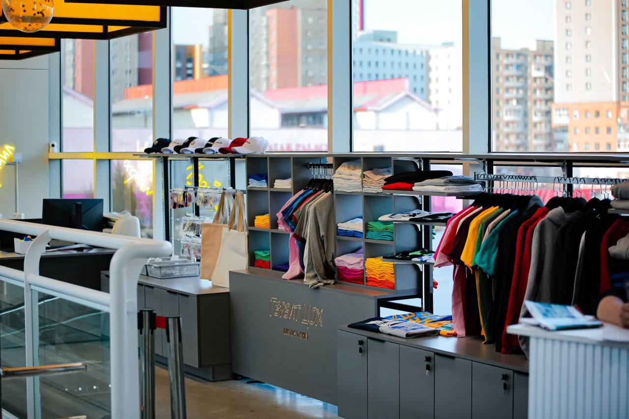 Цэвэрхэн эвхэж өлгөөтэй өнгө өнгийн хувцас, малгайнууд, гадаа хотын өнгө үзэмжийг харуулсан том цонхтой орчин үеийн жижиглэн худалдааны дэлгүүр. Орчин үеийн интерьер дизайнтай, гэрэлтүүлэг сайтай. - Business.MN