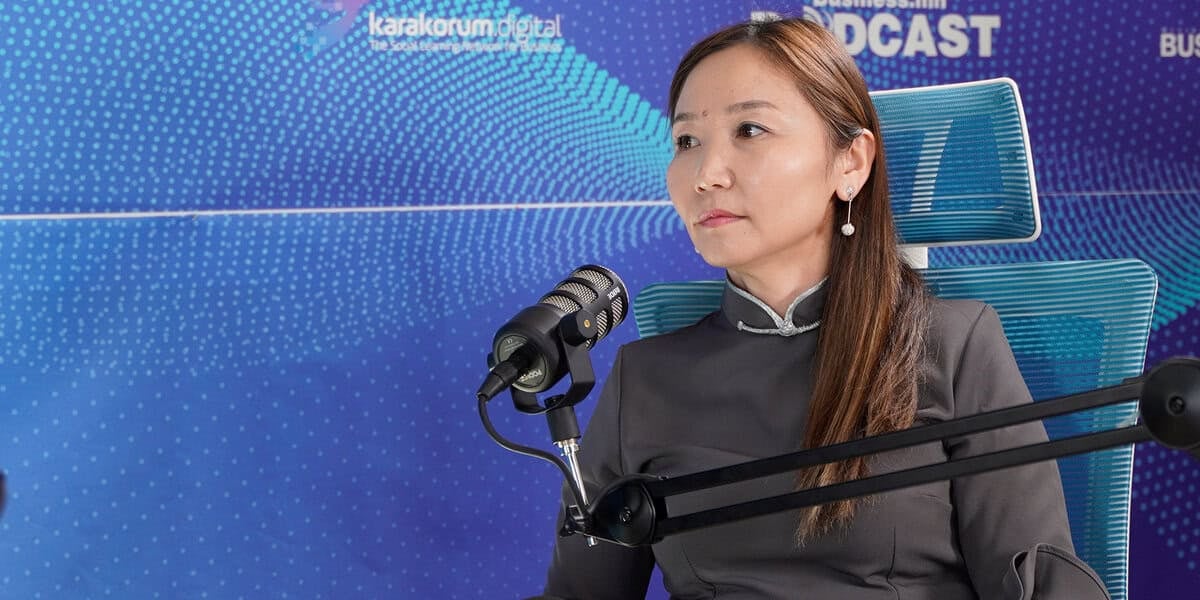 Урт үстэй эмэгтэй микрофоны өмнө цэнхэр сандал дээр сууж, мөнгөн дэвсгэрт бүхий бараан өнгийн уламжлалт хувцас өмссөн байна. Арын дэвсгэр дээр "Каракорум Дижитал ПОДКАСТ" гэсэн бичигтэй цэнхэр өнгийн тасархай загвартай. Энэхүү цэцэглэн хөгжиж буй энтрепренер өөрийн бизнес аялалын талаар чин сэтгэлээсээ ярилцдаг. - Business.MN