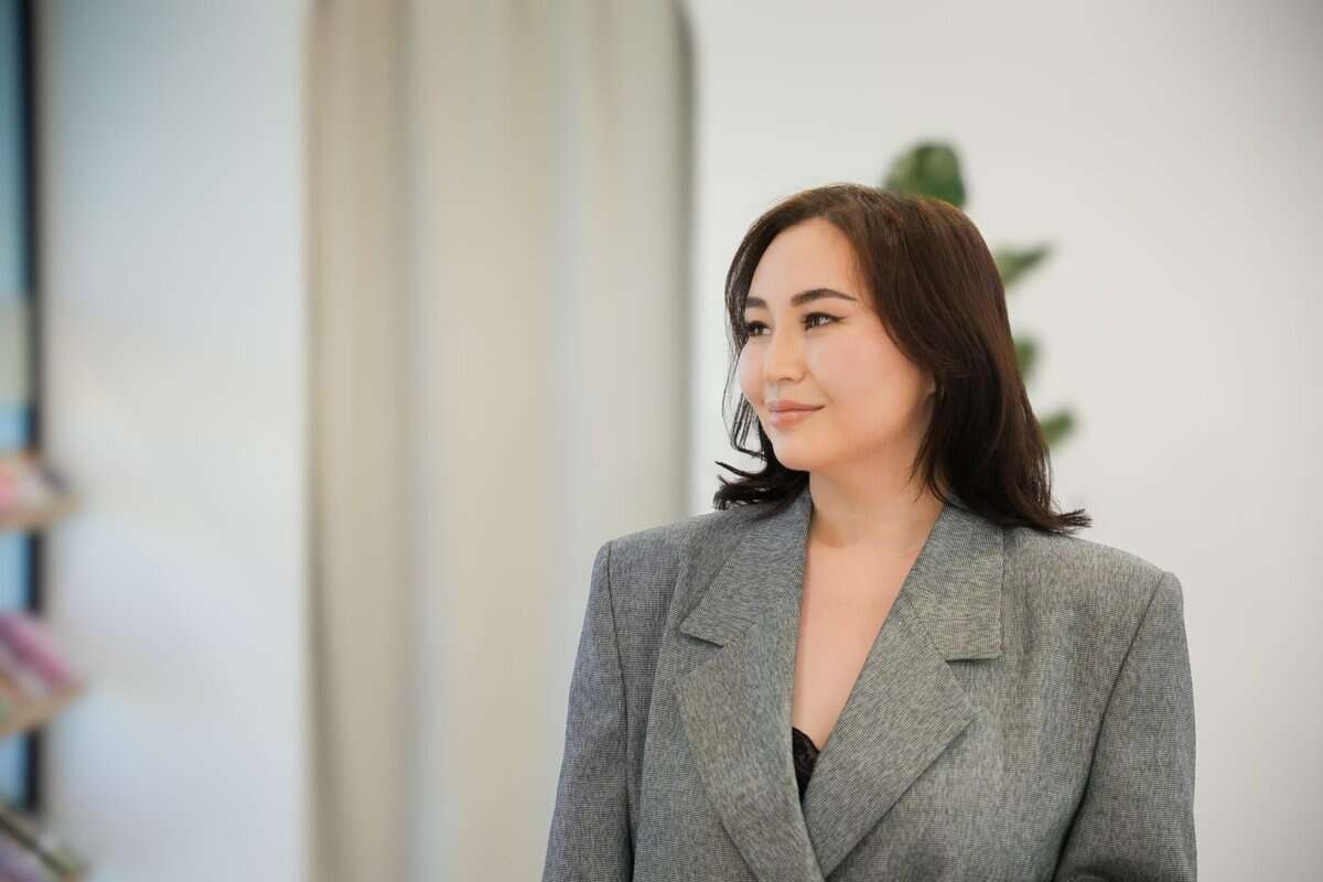 Мөр хүртлээ хар үстэй, арьсны ментор, саарал пиджак өмсөж, дотор нь зогсож байна. Арын дэвсгэр нь зөөлөн гэрэлтүүлэг, тодорхой бус элементүүдээр бүдгэрч, тайван уур амьсгалыг бүрдүүлдэг. - Business.MN