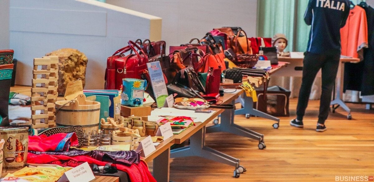 Дотор ширээн дээр цүнх, модон тоглоом, ороолт зэрэг гар хийцийн төрөл бүрийн бараанууд тавигддаг. Хажууд нь "Италиа" хүрэмтэй хүн зогсож байна. Цонхоор орж буй байгалийн гэрэл нь гэрэл гэгээтэй байдаг. - Business.MN