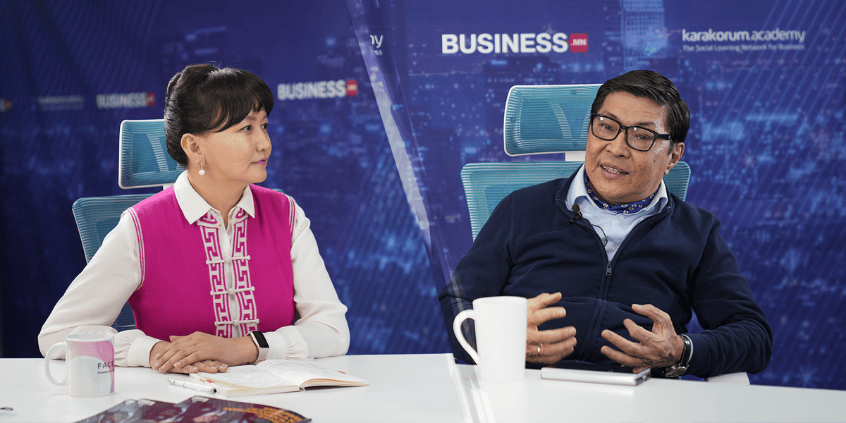 Студийн орчинд хоёр хүн ширээнд сууж байна. Зүүн талд байгаа эмэгтэй цагаан цамц өмссөн ягаан хантааз өмссөн бол баруун талд байгаа энтрепренер бололтой эрэгтэй хүн ярьж, нүдний шил зүүсэн байна. Арын дэвсгэр дээр "БИЗНЕС" гэсэн бичвэр болон бусад лого харагдаж байна. - Business.MN