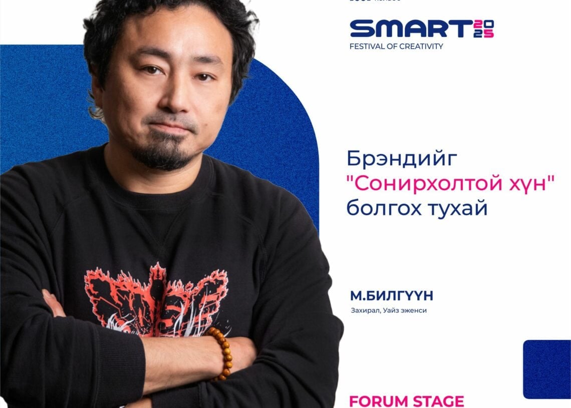 Хар буржгар үстэй, сахалтай эр улаан загвартай хар цамц өмссөн гараа зөрүүлэн зогсож байна. Бүтээлч байдлын SMART 2023 бүтээлч фестивальд түүний илтгэлийг Монгол, Англи хэлээр сурталчилж байна. - Business.MN