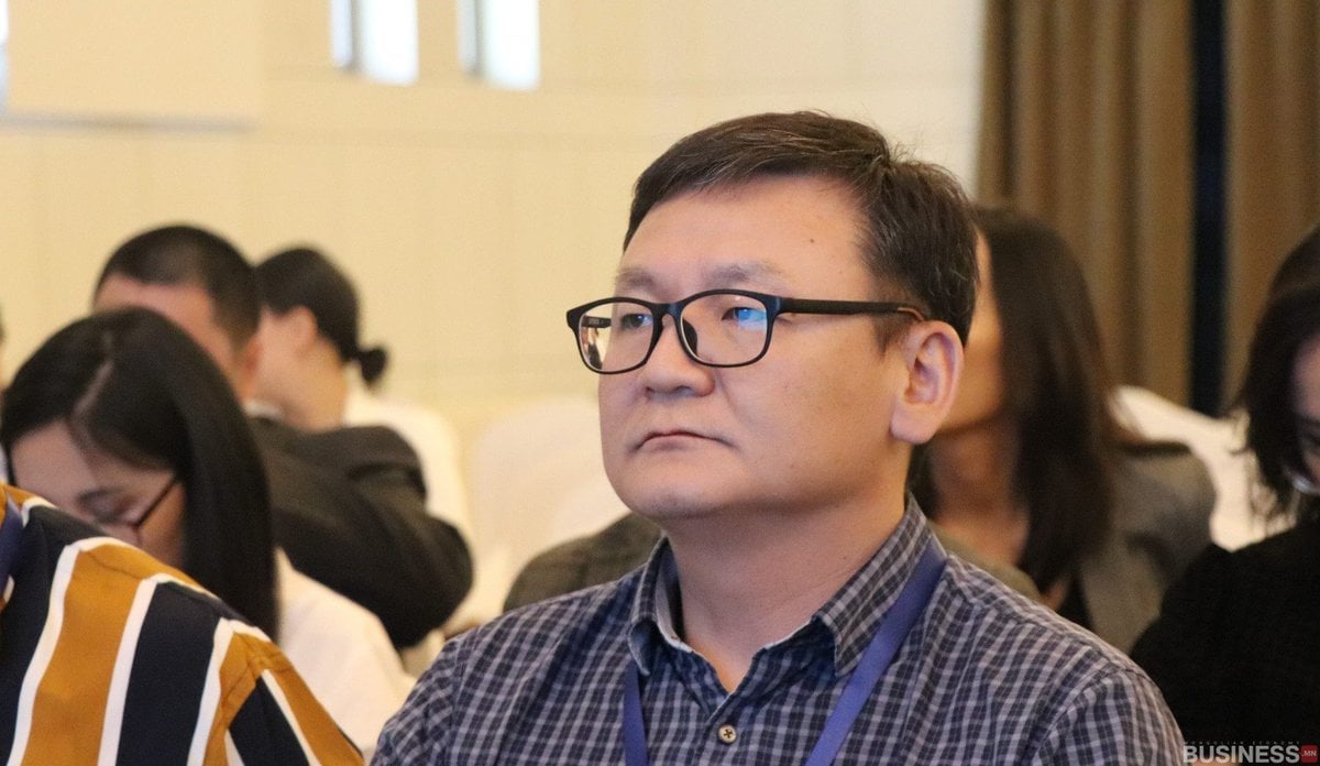 Нүдний шил, алаг цамц өмссөн хүн чуулганыг анхааралтай сонсож байна. Бусад оролцогчид анхаарал төвлөрөл, оролцоо холилдсон арын ард сууж байна. - Business.MN