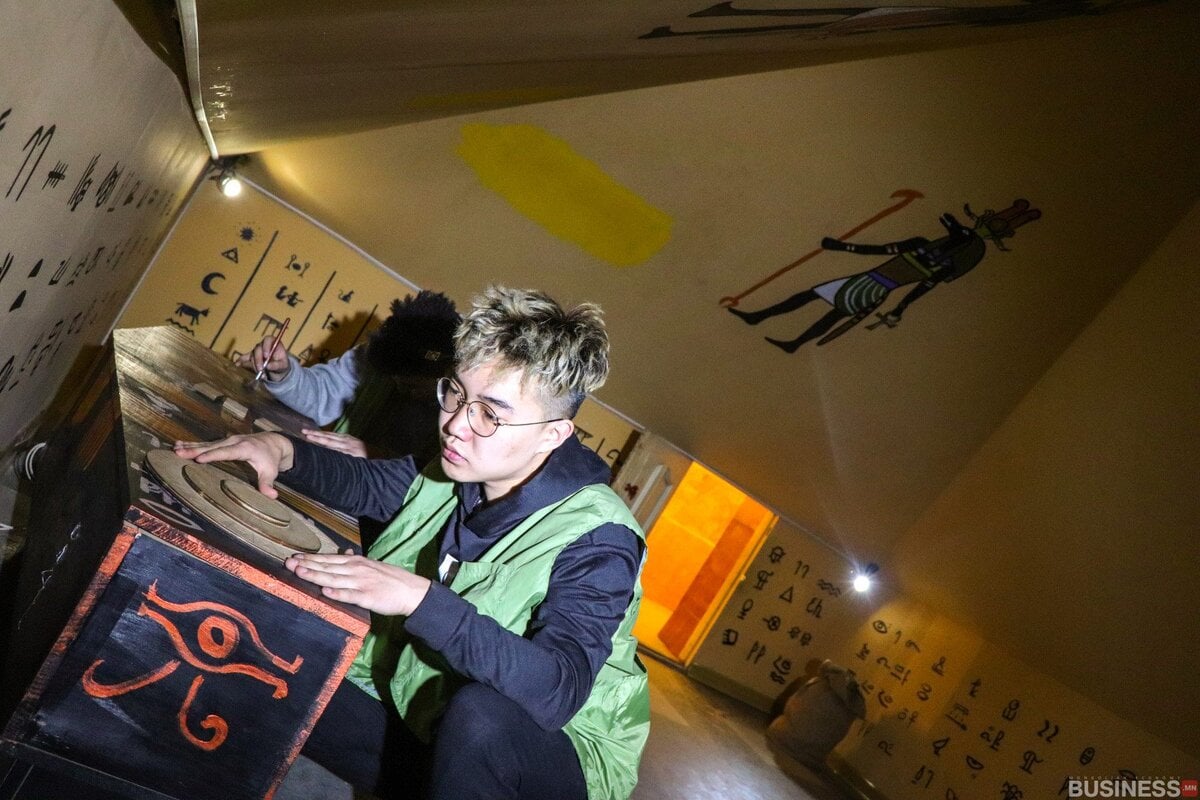 Египетийн сэдэвтэй зугтах өрөөнд байгаа хоёр хүн. Нэг нь иероглиф бүхий оньсогоын хайрцгийг шалгаж байхад нөгөө нь ханан дээр төвлөрч байгаа бололтой. Өрөө нь бүдэгхэн гэрэлтэй, Анубисын ханын зураг, ханан дээр янз бүрийн тэмдэгтүүдийг харуулсан. - Business.MN