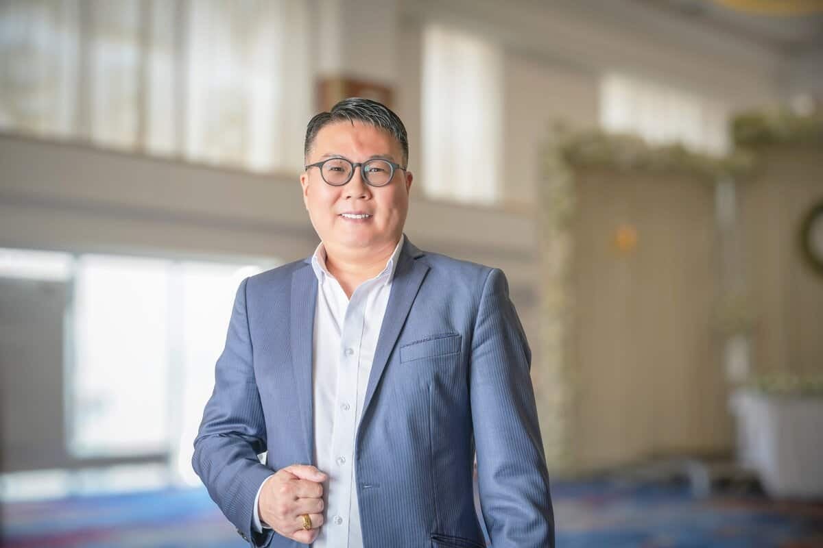 Нүдний шил, саарал костюм өмссөн хүн том цонхтой, гэрэлтүүлэг сайтай тасалгааны орчинд өөртөө итгэлтэй зогсож байгаа нь үйлчилгээний бизнесийн мэргэжлийн ур чадварыг илтгэнэ. Арын дэвсгэр нь зөөлөн бүдгэрч, ойр дотно уур амьсгалыг бүрдүүлдэг. - Business.MN