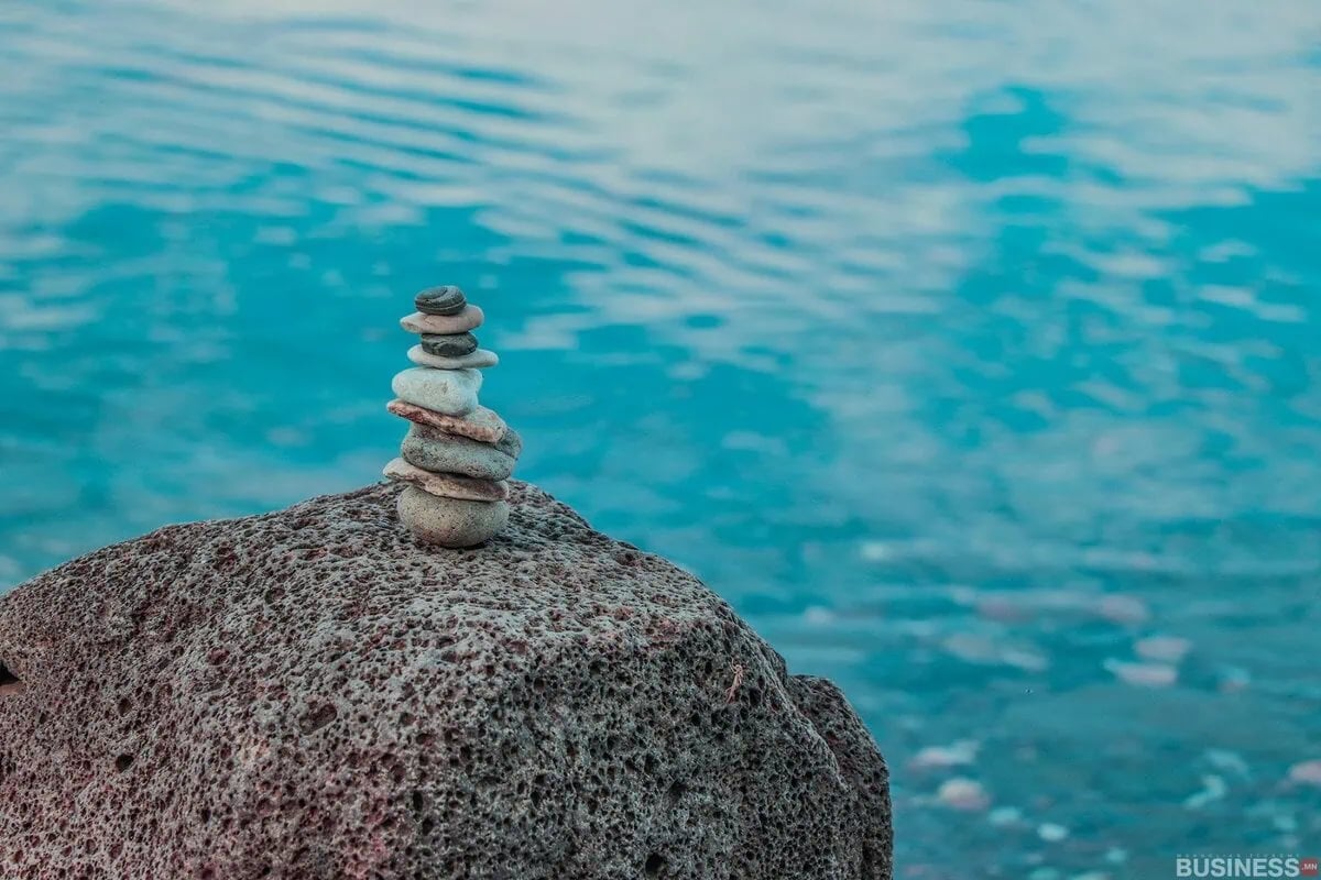 Гөлгөр чулуунуудын жижиг бөөгнөрөл нь тунгалаг цэнхэр усны ирмэг дээр том хадан дээр тэнцвэрждэг. Тайвширсан ус нь зөөлөн долгионтой бөгөөд тайван, тайван уур амьсгалыг бүрдүүлдэг. - Business.MN