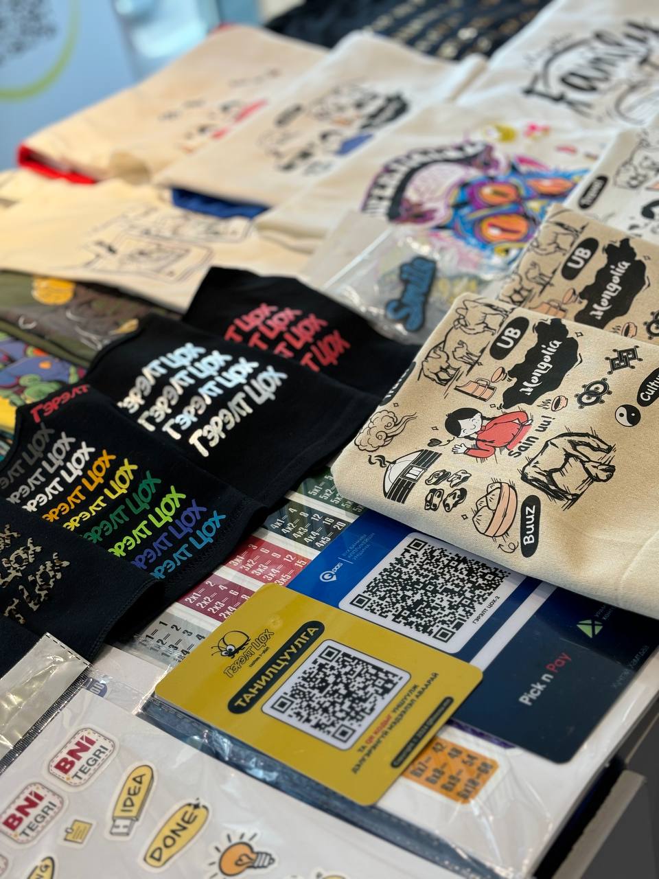 Хөгжилтэй текст, дүрслэл бүхий өнгөлөг график подволк, цүнх, наалт бүхий дэлгэцийн ширээ. QR код, нэрийн хуудас нь төлбөр тооцоо болон холбоо барих мэдээлэлд зориулагдсан болно. - Business.MN