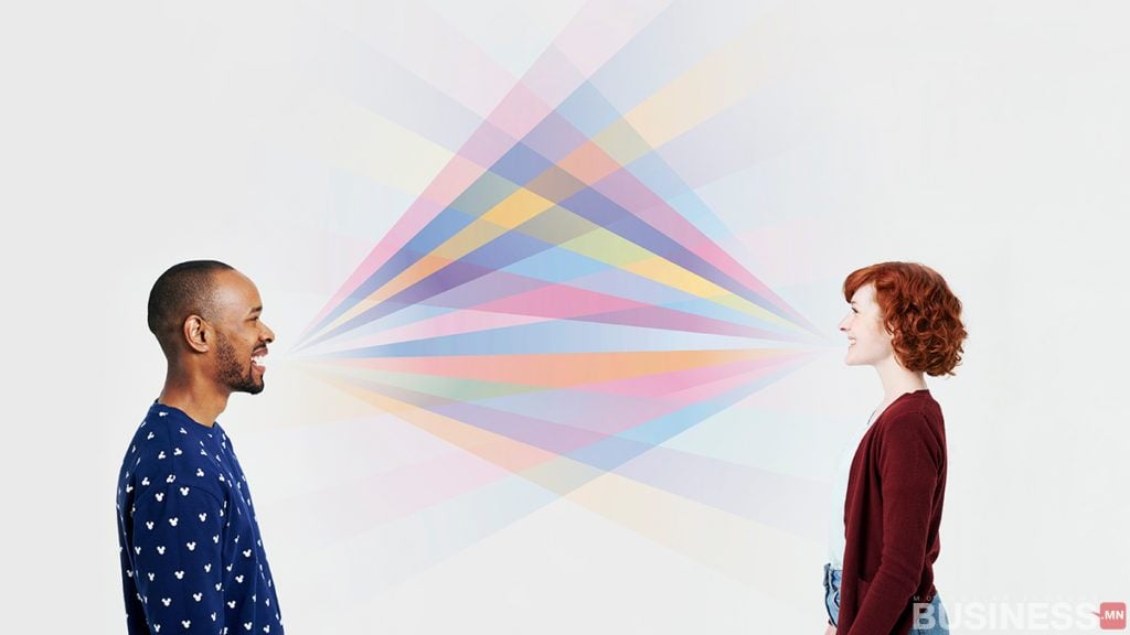 Эрэгтэй, эмэгтэй хоёр бие биенийхээ өөдөөс харж инээмсэглэн зогсоно. Тэдний амнаас давхцсан өнгөлөг гэрлийн цацрагууд гарч, өнгөт спектрийг үүсгэдэг. Арын дэвсгэр нь дуугүй саарал өнгөтэй бөгөөд эрч хүчтэй туяаг тодотгож өгдөг. - Business.MN