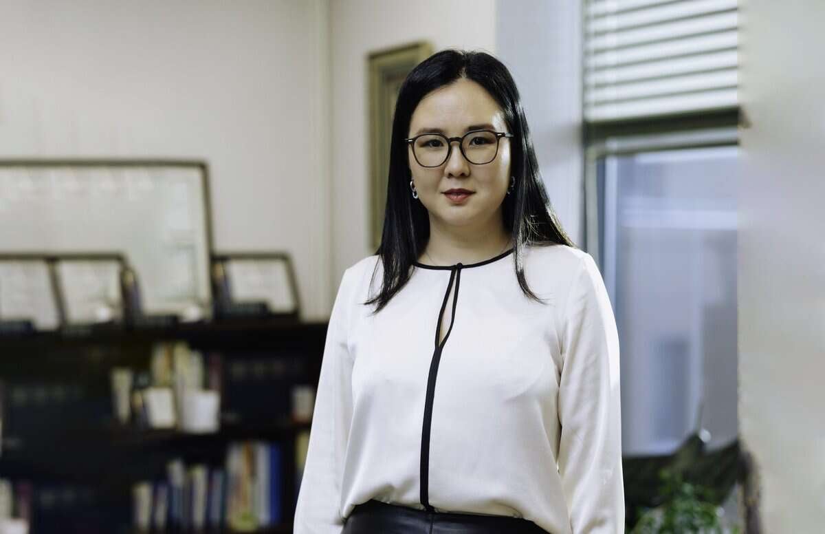 Урт хар үстэй, нүдний шилтэй эмэгтэй цагаан цамц, хар өмд өмссөн оффист зогсож байна. Өрөөний ханан дээр жаазтай гэрчилгээ, цаана нь номын тавиурууд байдаг. Тэрээр компанийг амжилтанд хүргэхэд бэлэн энтрепренерийн мөн чанарыг тусгасан төвийг сахисан илэрхийлэлтэйгээр камерын өмнө тулгардаг. - Business.MN