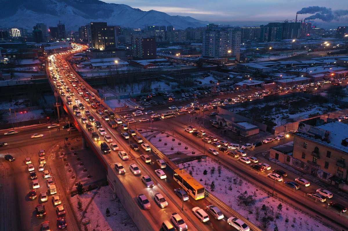 Бүрэнхий үед хөл хөдөлгөөн ихтэй хотын агаараас харахад хоёр зам, гүүрэн дээр ачаалал ихтэй байгааг харуулж байна. Хөгжин цэцэглэж буй компаниуд болон үйлдвэрийн газруудын олон тооны барилга байгууламжууд цаана нь уулстай харагдана. Цас газрыг бүрхэж, энэ газарт өвлийн уур амьсгал нэмдэг. - Business.MN