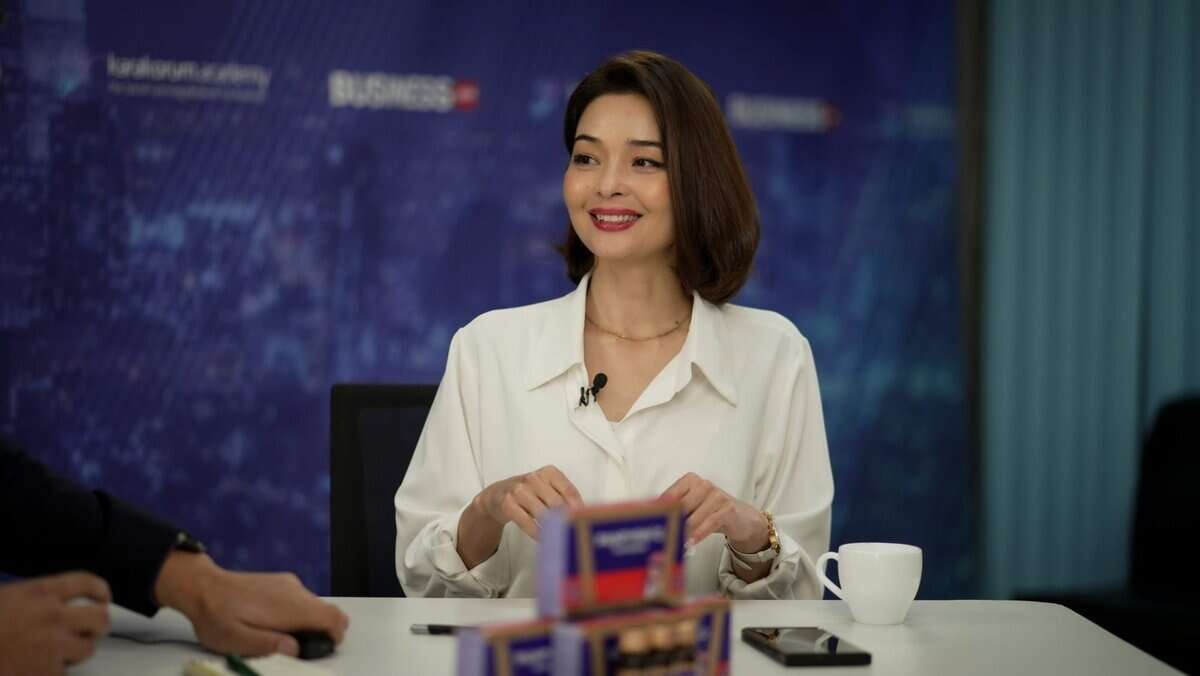 Мөр хүртлээ урт бор үстэй, цагаан цамц өмссөн эмэгтэй аяга кофе, хэдэн хайрцагтай ширээний ард сууж байна. Арын дэвсгэр дээр "Бизнес" гэсэн бичигтэй цэнхэр хотын өнгө үзэмжийг харуулсан байна. Тэрээр инээж, камерын бусаар харж, компаниа хөгжүүлэхэд бэлэн энтрепренерийн сүнсийг шингээдэг. - Business.MN