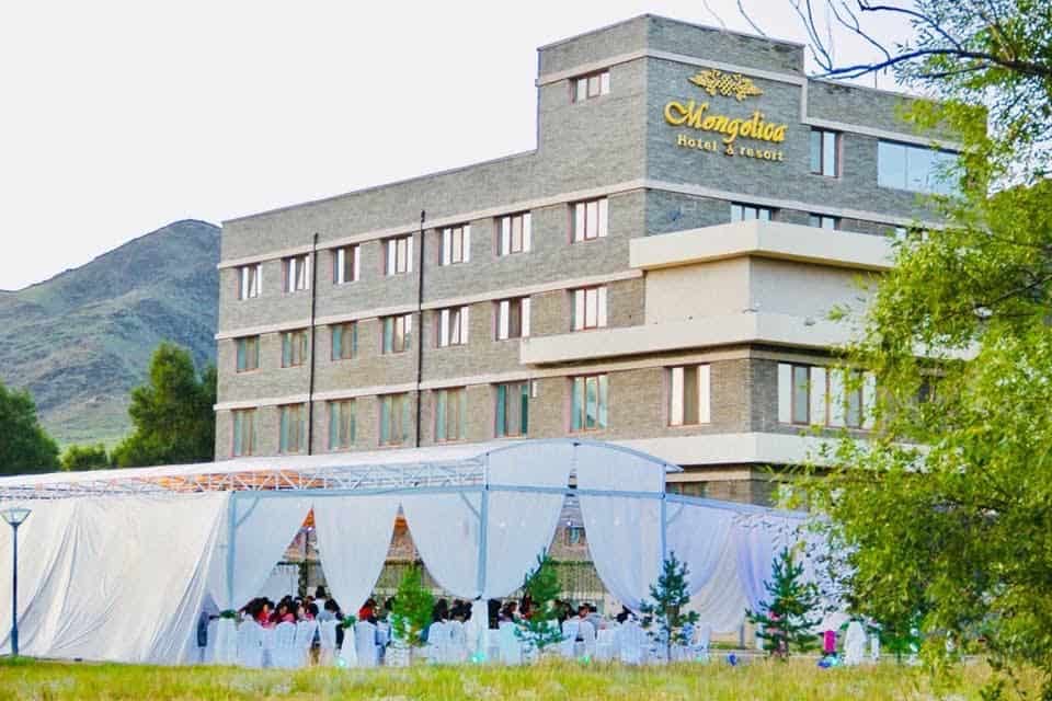 "Mongolica Hotel & Resort" гэсэн шошготой олон давхар тоосгон барилга уулархаг газар, эргэн тойронд нь модоор хүрээлэгдсэн байдаг. Урд талд нь орон нутгийн бизнес эрхлэгчдийн зохион байгуулж буй арга хэмжээнд зориулж том цагаан майхан барьж, ширээ сандлаа засаж, майхны доор зочдыг суулгажээ. - Business.MN