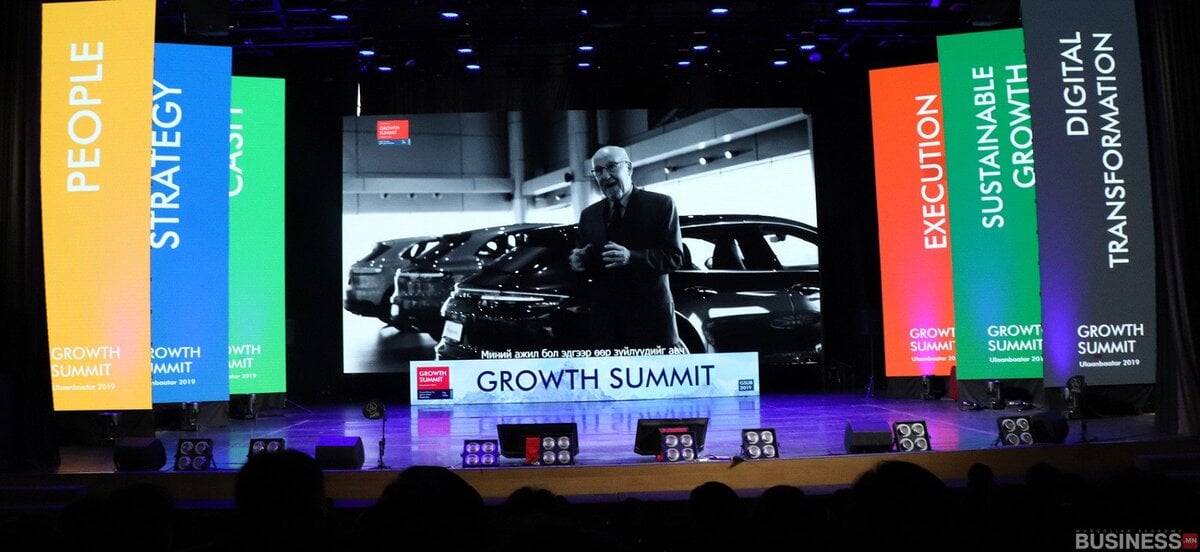 Бизнес хурлын тайз нь илтгэгчийг харуулсан том дэлгэцтэй бөгөөд үйл явдлын сэдвүүдийг харуулсан өнгөлөг баннерууд, бизнес эрхлэгчдийн ойлголтыг онцолсон байдаг. - Business.MN