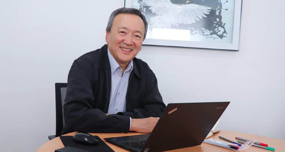 Инээмсэглэж буй эр ширээний ард суугаад зөөврийн компьютер, төрөл бүрийн эд зүйлс барин, энтрепренерийн эрч хүчтэй эрч хүчийг харуулж, ханан дээр нь урлагийн бүтээлүүд тавьж байна. - Business.MN