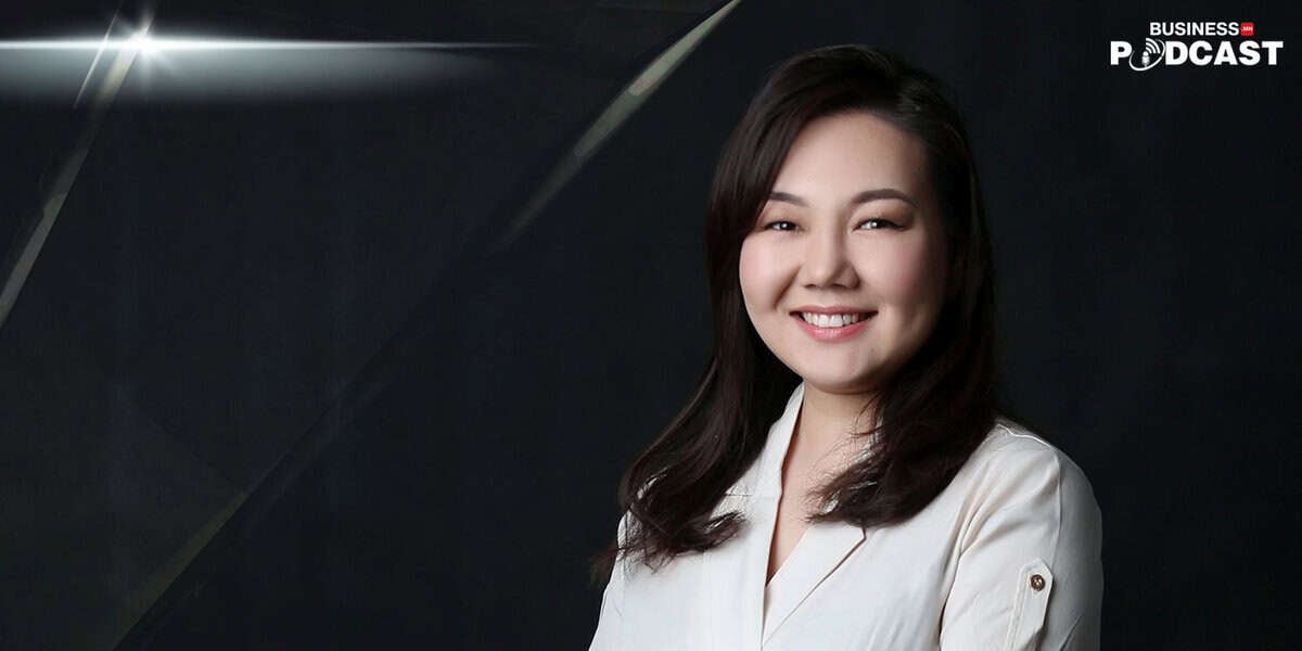 Урт хар үстэй, цайвар өнгийн цамц өмссөн инээмсэглэсэн хүн бараан дэвсгэр дээр зогсож байна. Зургийн баруун дээд буланд "Бизнесийн Подкаст" гэсэн үгс гарч ирсэн нь тэдний компани болон энтрепренерүүдийн амжилтын түүхийг онцлон харуулж байна. - Business.MN