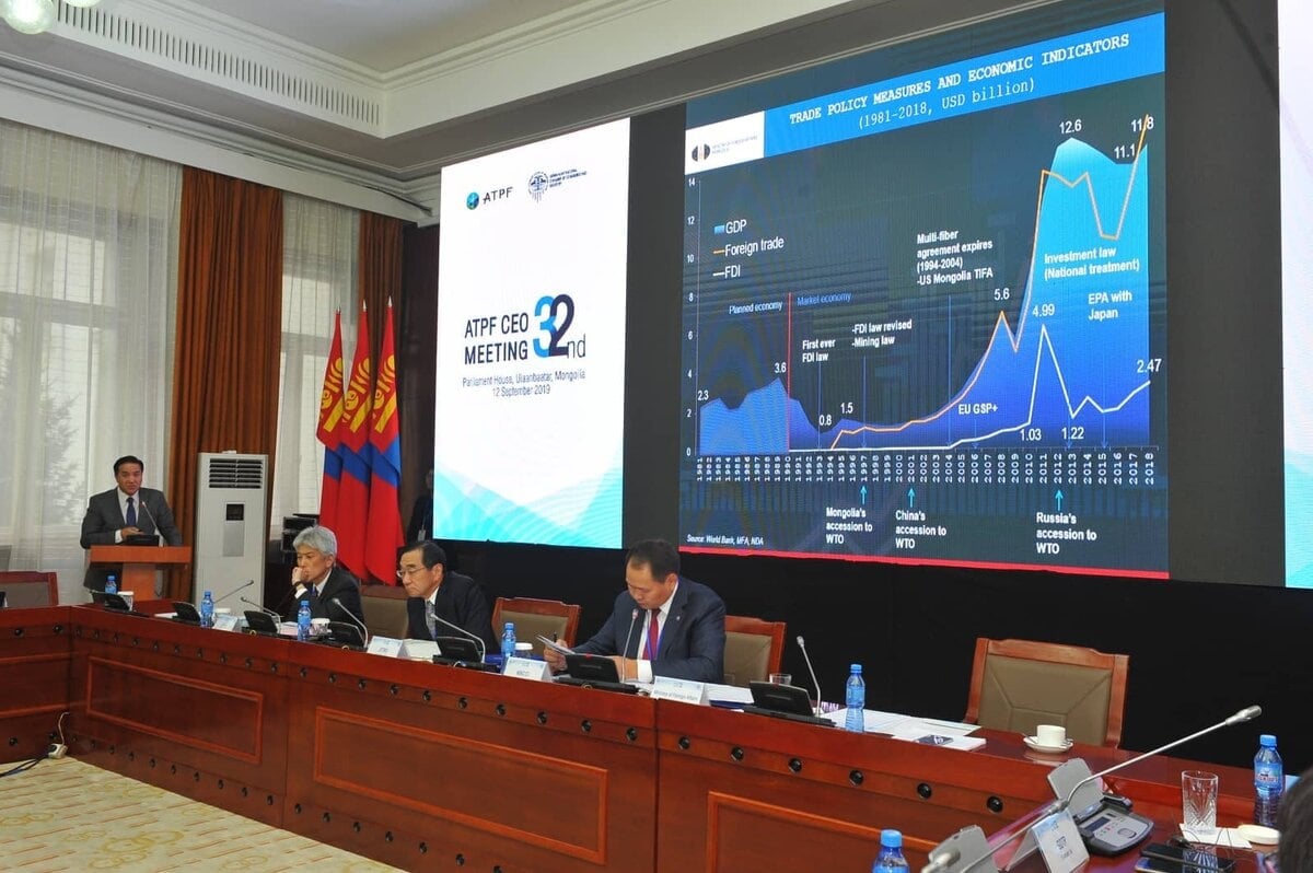 Урт ширээн дээр хэдэн хүн суусан хурлын танхим. Том дэлгэцэн дээр худалдааны бодлогын арга хэмжээ, эдийн засгийн үзүүлэлтүүд, Монгол, Япон хоёр улсын худалдааны мэдээллийн график зэрэг танилцуулгыг үзүүлжээ. Туг, лого харагдаж байна. - Business.MN