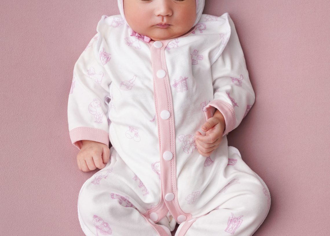 Ягаан өнгийн хээтэй цагаан өмд өмсөж, жижигхэн чихтэй малгай өмссөн хүүхэд ягаан гадаргуу дээр тайван унтаж байна. - Business.MN