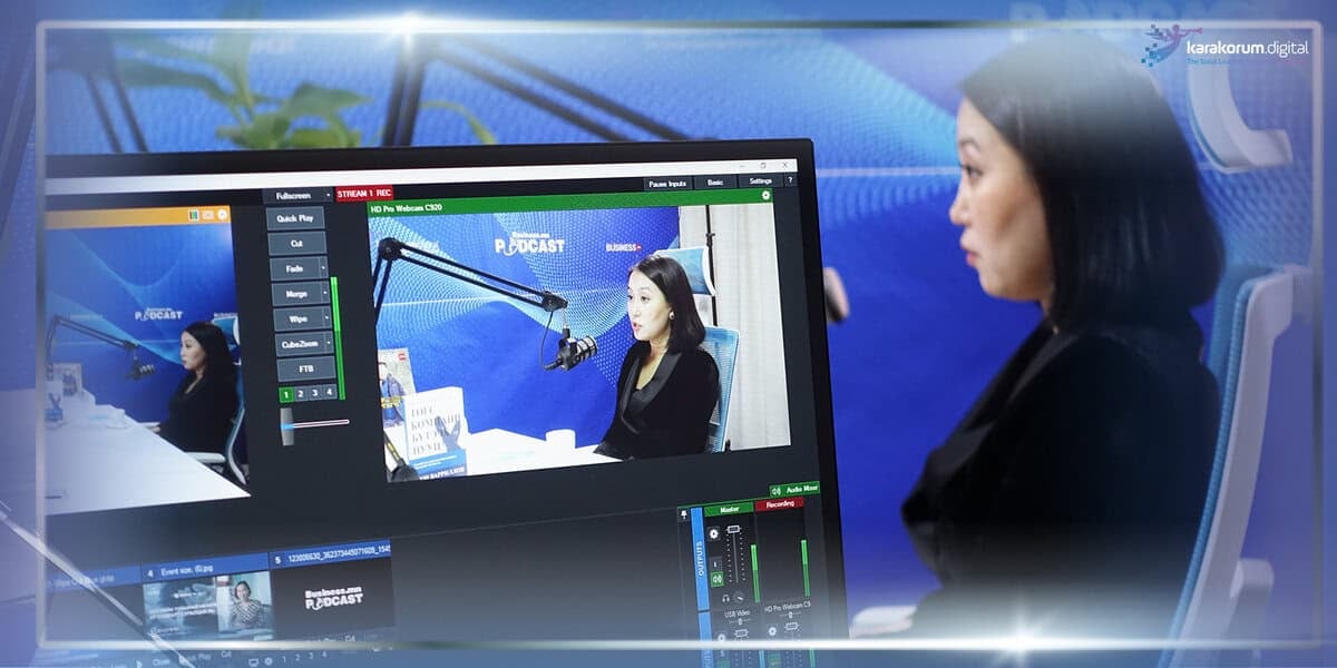 Нэг эмэгтэй подкаст студид микрофоны өмнө сууж, түүний зургийг компьютерийн дэлгэц дээр харуулж, бизнесийн сүүлийн үеийн чиг хандлагын талаар ярилцаж байна. - Business.MN