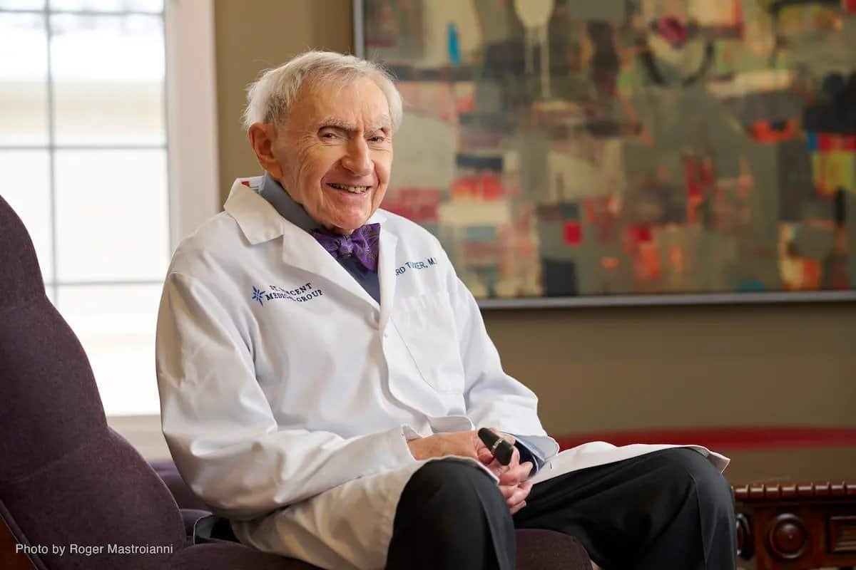 Лабораторийн цагаан цув өмссөн өндөр настан сандал дээр инээмсэглэн сууж байна. Тэд зүүн гартаа хар юм шиг харагддаг зүйлийг барьдаг. Цаана нь ханан дээр хийсэн хийсвэр зураг, байгалийн гэрэл оруулах том цонх байдаг нь энтрепренерт тохирсон урам зориг өгөх уур амьсгалыг бүрдүүлдэг. - Business.MN