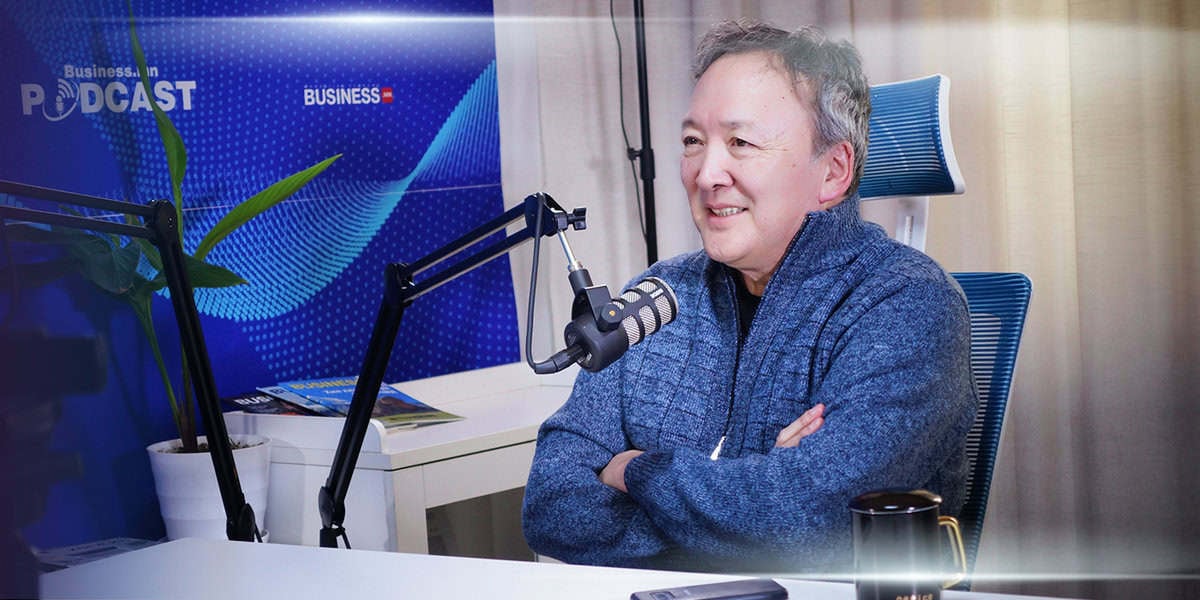 Подкастингийн студид микрофон бариад ширээний ард сууж бизнес болон энтрепренерийн аяллын талаар үнэ цэнэтэй санаагаа хуваалцаж буй хүн инээмсэглэж байна. - Business.MN