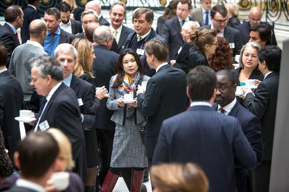 Албан ёсны цугларалт дээр ажил хэрэгч хувцастай том бүлэг хүмүүс холилдон, чатлаж байна. Тэд аяга барьж, яриа өрнүүлж байгаа харагдана. Энэхүү тохиргоо нь өргөн, гэрэлтүүлэг сайтай өрөөнд сүлжээний арга хэмжээ эсвэл бага хуралтай төстэй юм. - Business.MN