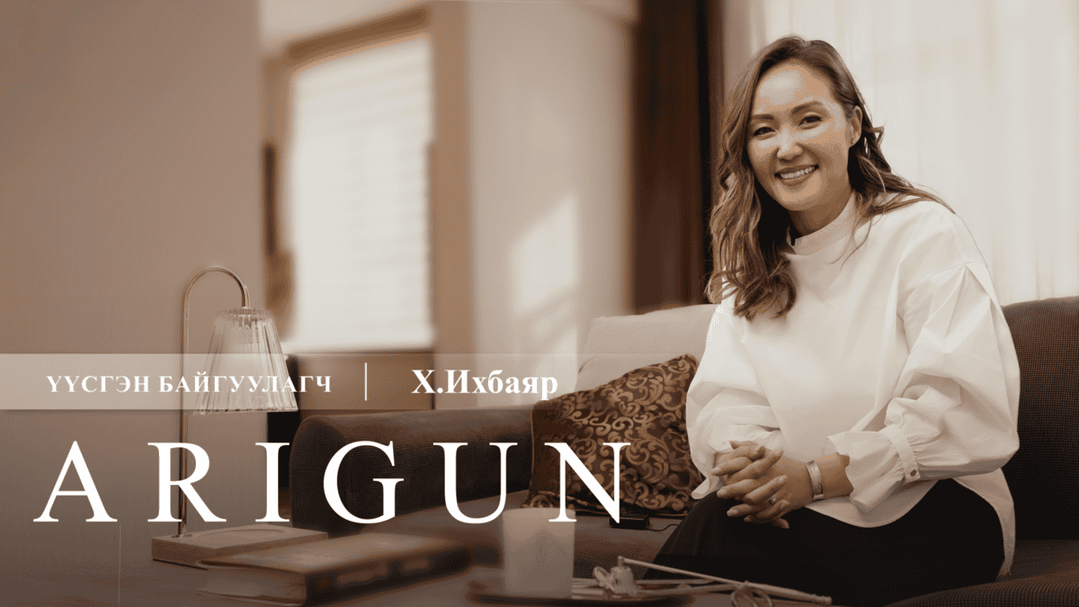 Долгион үстэй, цагаан цамц, бараан өмд өмссөн эмэгтэй гэрэлтүүлэг сайтай өрөөнд буйдан дээр сууж байна. Тэр инээмсэглэж, өмнө нь ширээн дээр ном, дэнлүү тавьсан байна. Уг бичвэрт "Энтрепренер Үүсгэн Байгуулагч | Х.Ихбаяр ARIGUN. - Business.MN