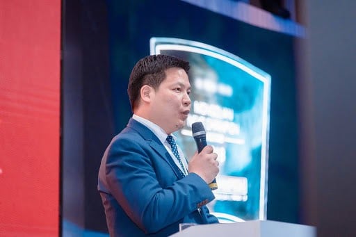 Цэнхэр костюмтай бизнес эрхлэгч компанийхаа амжилтыг харуулсан том дэлгэцтэй хурлын үеэр микрофонд ярьж байна. - Business.MN