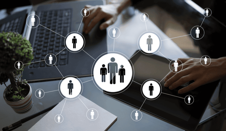 Бизнесийн хүн сүлжээний диаграмм давхардсан зөөврийн компьютер болон таблет дээр ажиллаж байна. Диаграм нь хүмүүсийг дүрсэлсэн, шугамаар холбогдсон, багаар ажиллах эсвэл нийгмийн сүлжээг санал болгодог дүрсүүдээс бүрдэнэ. Ширээн дээр жижиг ургамал, тэмдэглэлийн дэвтэр бас харагдаж байна. - Business.MN