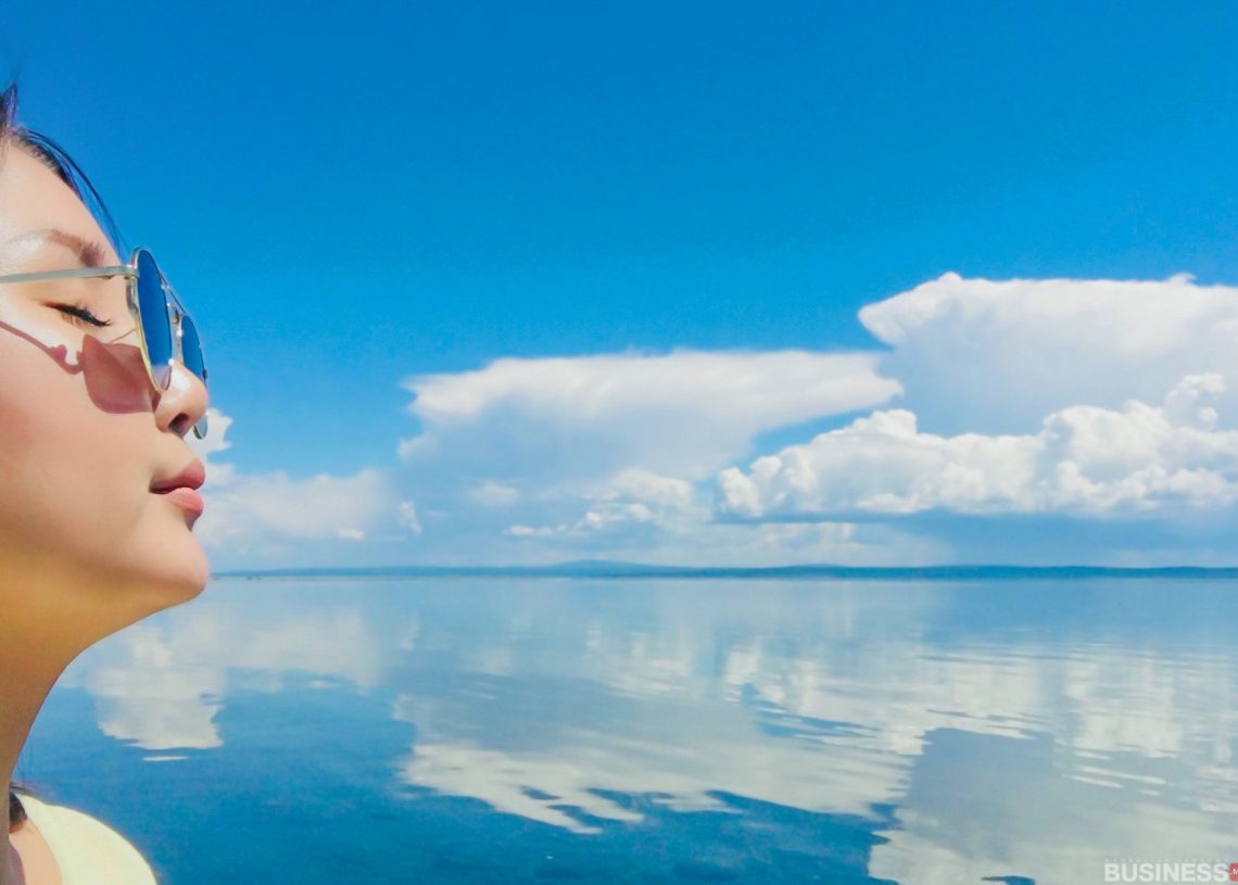 Нарны шил зүүсэн хүн өргөн уудам усны дэргэд тунгалаг өдрийг зугаатай өнгөрүүлж байна. Тэнгэр цэнхэр өнгөтэй, сэвсгэр цагаан үүлс нь усны тайван гадаргуу дээр тусна. - Business.MN