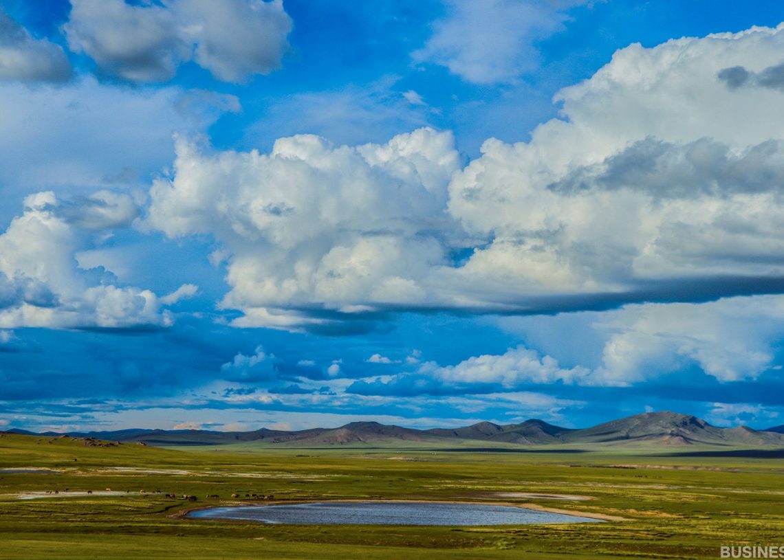 Том сэвсгэр үүл бүхий тод хөх тэнгэрийн дор ногоон тал нутгаар хүрээлэгдсэн жижиг нуур бүхий өргөн уудам газар нутаг. Алсын уулс тэнгэрийн хаяанд харагдана. - Business.MN