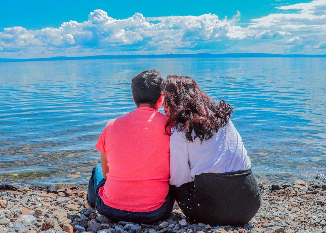 Хосууд хад чулуурхаг эрэг дээр ойрхон сууж, үүл бүрхсэн тод цэнхэр тэнгэрийн дор тайван, өргөн уудам нуурыг харж байна. Зүүн талд байгаа хүн улаан цамц өмсдөг бол баруун талд байгаа хүн цагаан дээд, хар банзал өмсдөг. - Business.MN