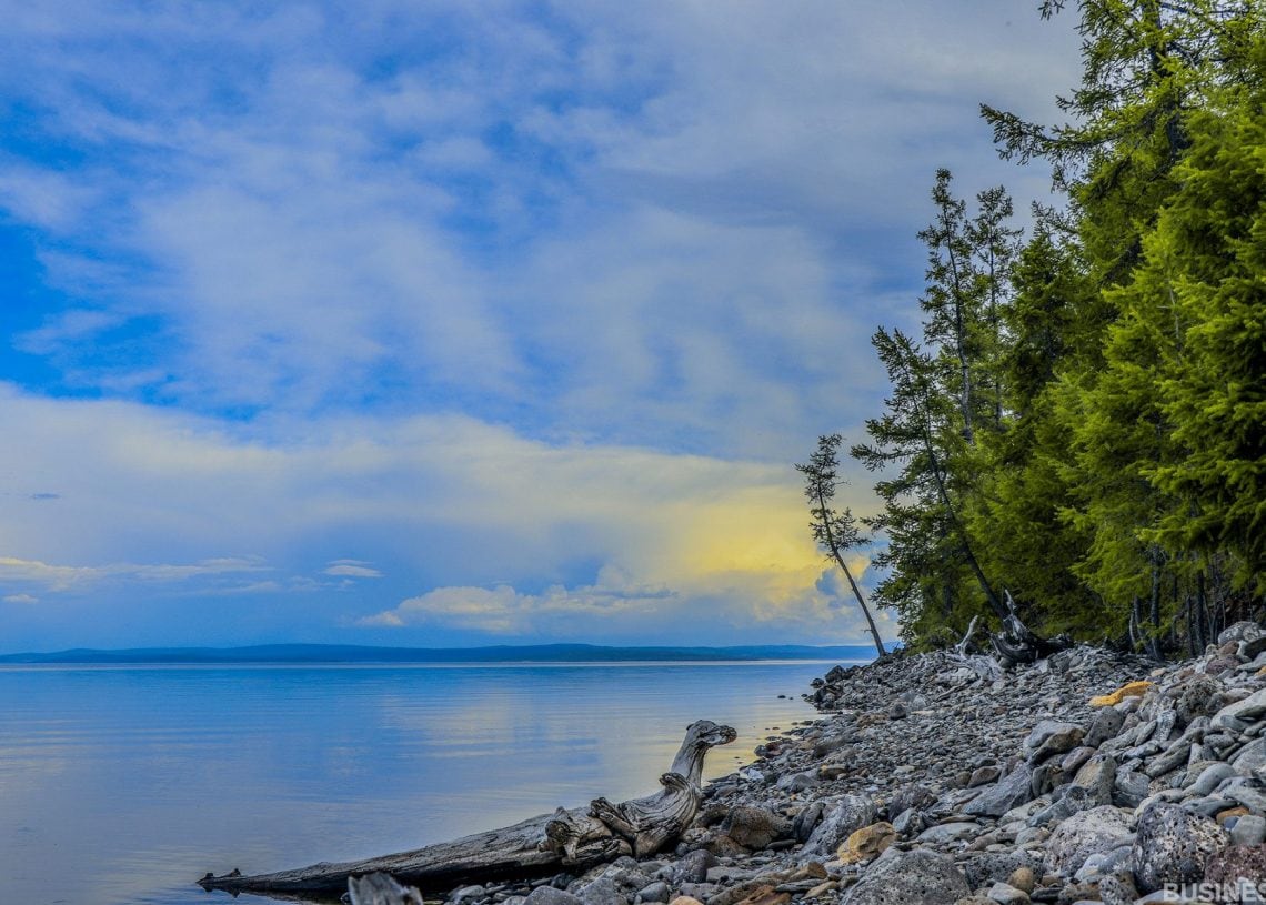 Намуухан устай, хад чулуурхаг эрэг бүхий нам гүм нуурын эргийн ландшафт. Хадан дээр дрифтвүүд хэвтэж байхад эрэг дээр өтгөн мөнх ногоон моднууд эгнэнэ. Цэнхэр өнгийн толбо бүхий уудам, үүлэрхэг тэнгэр дээшээ сунаж тогтоно. - Business.MN