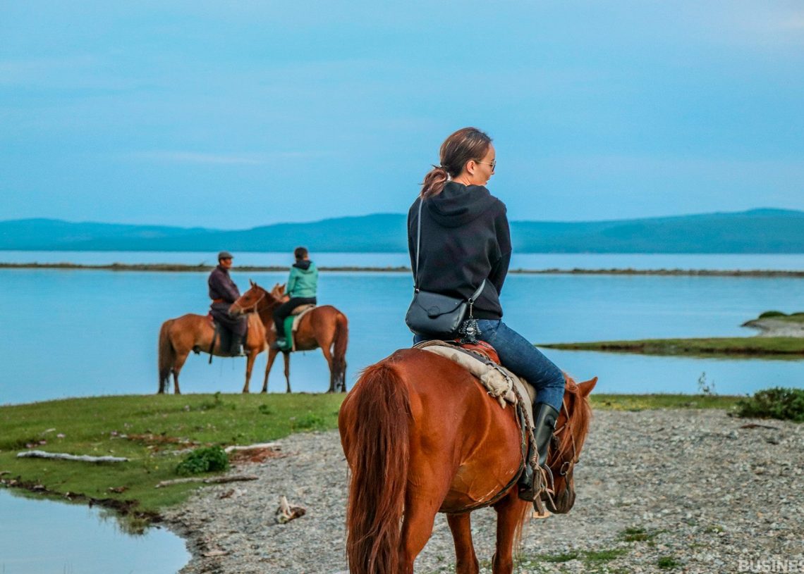 Хүрэн морьтой хүн намуухан нуурын өөдөөс харж, цаана нь хоёр морьтой хүн байна. Цэлмэг хөх тэнгэрийн дор ногоон зүлэг, алс холын толгодтой энэ үзэгдэл тайван амгалан. - Business.MN