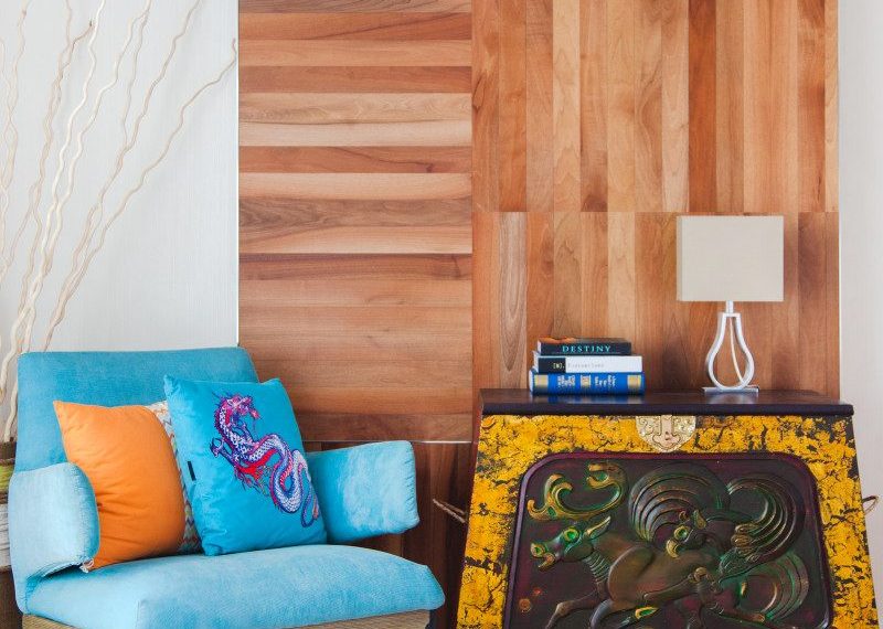 Орчин үеийн интерьер нь өнгөлөг дэр бүхий цэнхэр өнгийн түшлэгтэй сандал, гоёмсог дизайнтай модон консол ширээ юм. Ширээн дээр овоолсон номнуудын хажууд жижигхэн чийдэн сууна. Ханан дээр модон хавтантай, цагаан хивс шалан дээр хэсэгчлэн харагдаж байна. - Business.MN