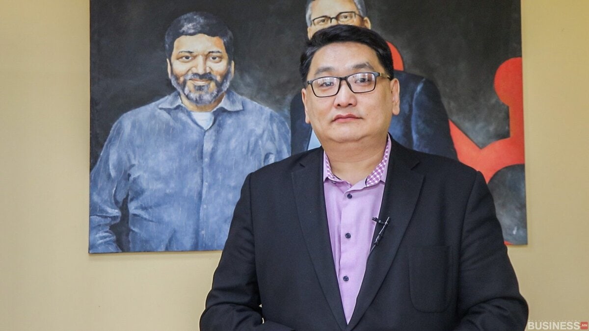 Хар пиджак, нил ягаан цамц өмссөн эр хоёр эрэгтэй хүний дүрс бүхий зургийн өмнө итгэлтэйгээр зогсоно. Арын дэвсгэр нь зөөлөн шар хана юм. - Business.MN