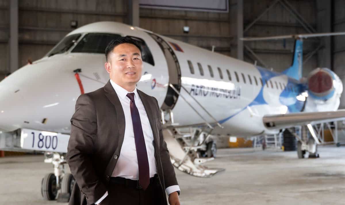 Харанхуй костюмтай эр нисэх онгоцны ангар дотор цагаан, цэнхэр онгоцны өмнө итгэлтэй зогсож байна. Онгоцон дээрээ "Аэро Монголиа" гэж бичсэн нь түүний компанийг хөгжүүлэхийн төлөө зүтгэж байгааг онцолсон байна. Арын дэвсгэр дээр ангарын үйлдвэрлэлийн нарийн ширийн зүйлийг харуулсан бөгөөд энэ нь түүний энтрепренер сэтгэлийг онцолж байна. - Business.MN