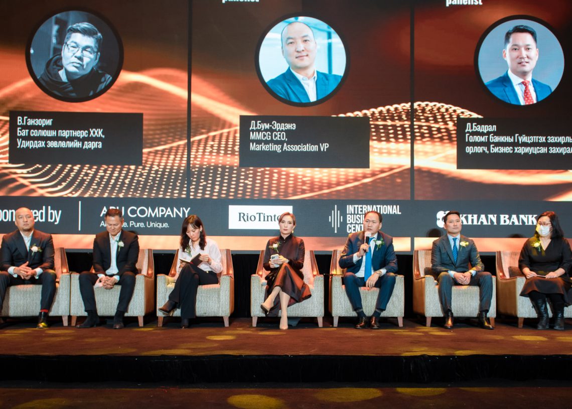 Дөрвөн эрэгтэй, хоёр эмэгтэй зургаан хүний бүрэлдэхүүнтэй баг албан ёсны ажил хэргийн хувцас өмссөн тайзан дээр эгнүүлэн сууна. Тэдний ард том дэлгэцэн дээр хэлэлцүүлэгт оролцогчдын гэрэл зураг, нэрсийг цол хэргэм, холбоотой компаниудын хамт харуулдаг. Үзэгчид урд талд бараг харагдахгүй байна. - Business.MN