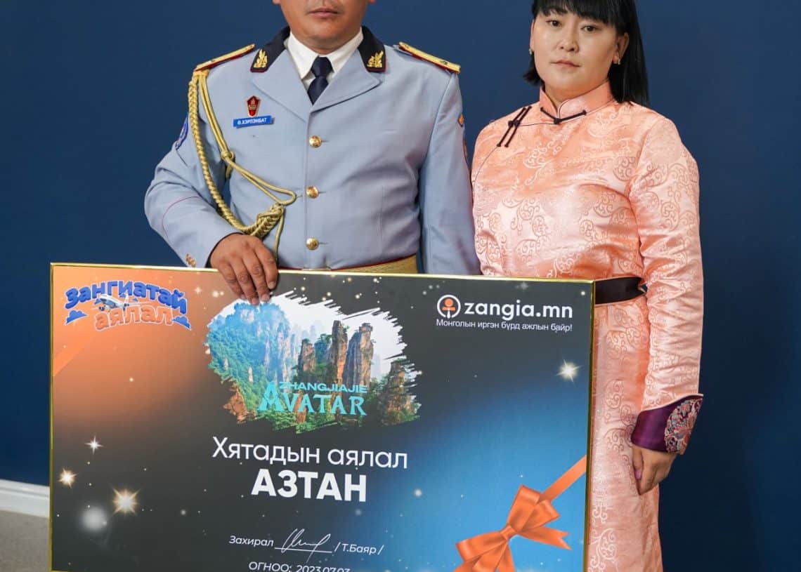 Цэргийн хувцастай эрэгтэй, үндэсний хувцастай эмэгтэй хоёр том шагналын карт барин зогсоно. Картан дээрх бичвэрт "Аватар", "Zangia.mn" гэсэн үгс бичигдсэн байна. Хоёулаа цэнхэр дэвсгэрийн өмнө зүүн дээд буланд логотой, бизнес болон компанийнхаа амжилтыг тэмдэглэж байна. - Business.MN