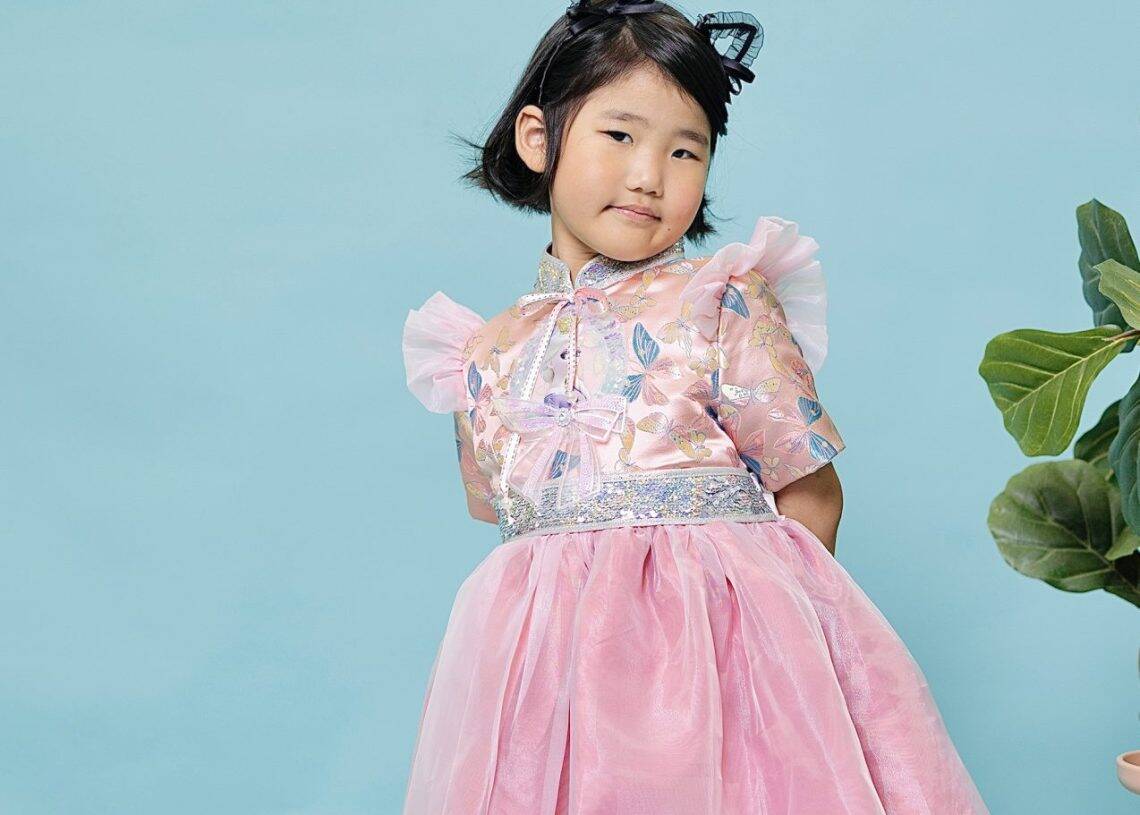 Бага насны хүүхэд цайвар цэнхэр дэвсгэрийн эсрэг зурж байна. Тэд цагаан трикотой хосолсон ханцуйтай ягаан, мөнгөн даашинз өмссөн байна. Муурны чихтэй хар тууз нь хөгжилтэй мэдрэмж төрүүлдэг. Ойролцоох хэсэгт ногоон навчит ургамал хэсэгчлэн харагдаж байгаа нь байгалийн бизнесийг илтгэж байна. - Business.MN