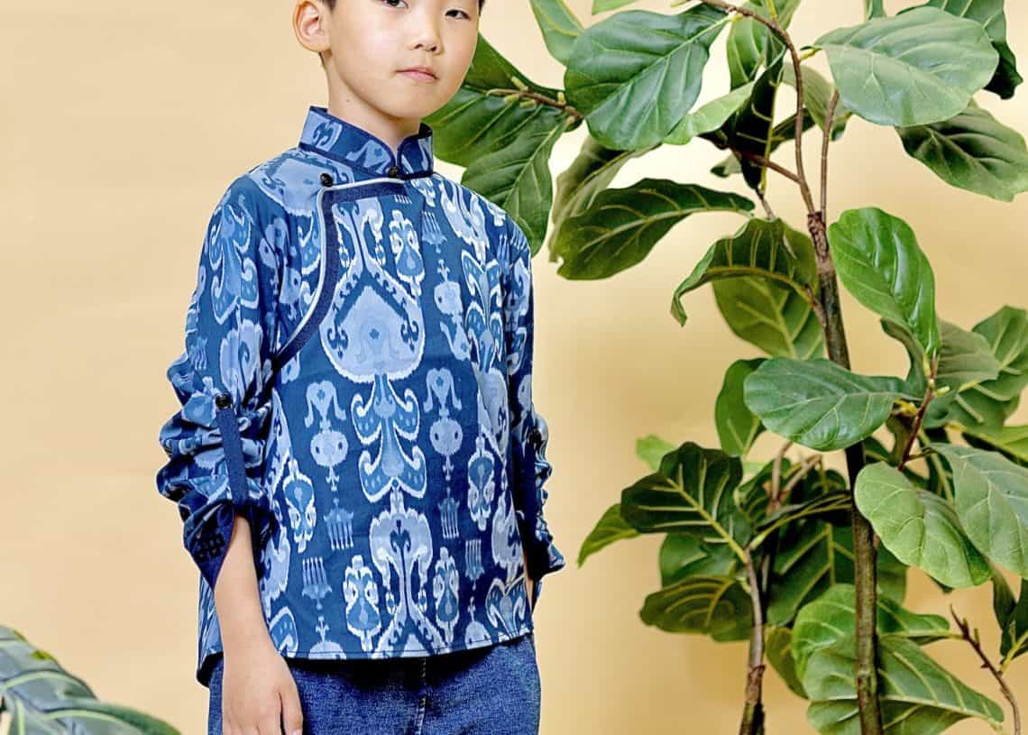 Залуу хүү том ногоон ургамлын дэргэд шаргал дэвсгэрийн өмнө итгэлтэйгээр зогсож байна. Цэнхэр хээтэй цамц, цэнхэр жинсэн өмд өмссөн тэрээр ирээдүйн энтрепренерийн тайван, өөртөө итгэлтэй байдлыг илтгэнэ. - Business.MN