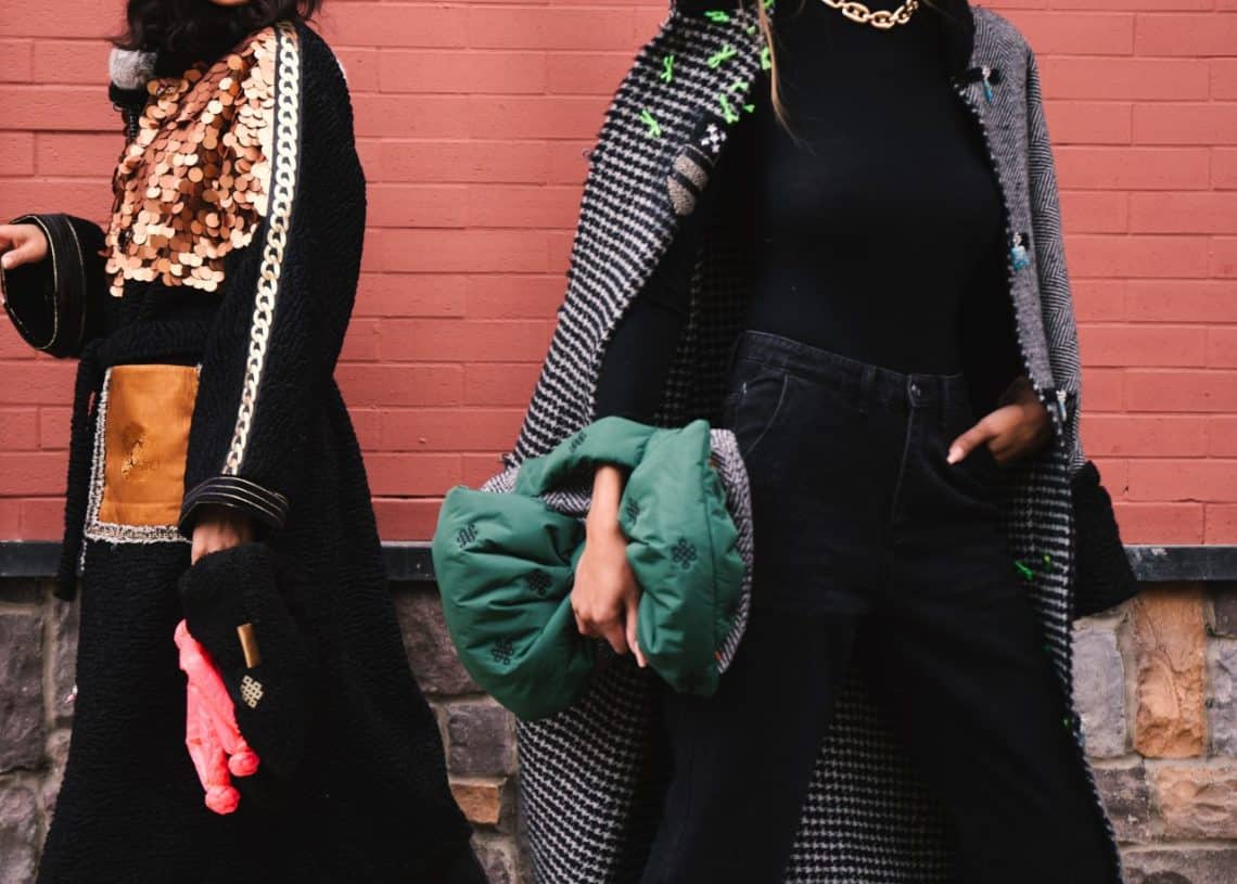 Бизнесийн ур чадварыг харуулсан хоёр загварлаг эмэгтэй тоосгон ханан дээр зогсож байна. Нэг нь хар малгай, нарны шил, алтаар чимэглэсэн хар хүрэм өмсдөг. Нөгөө нь өргөн хүрээтэй малгай, алаг малгай, хар яст өмд, хар жинсэн өмд өмсөж, ногоон жийргэвчтэй дагалдах хэрэгсэлтэй. - Business.MN