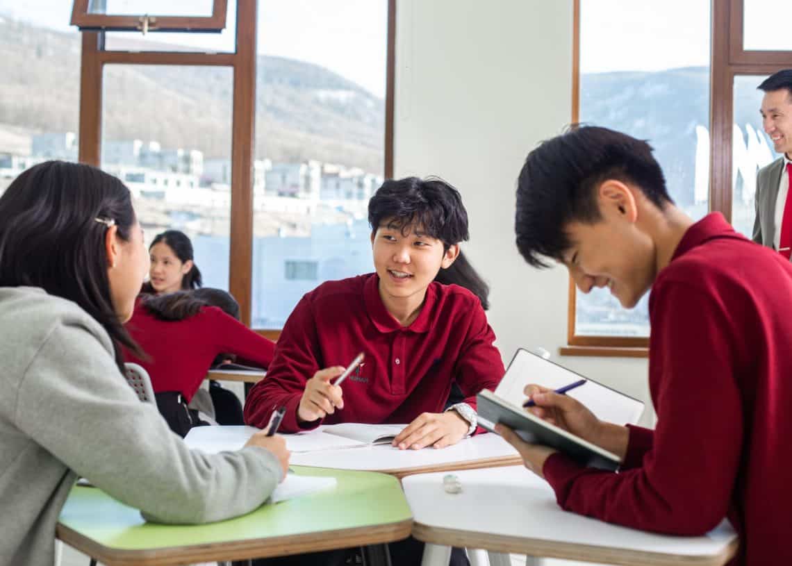 Хэсэг оюутнууд гэрэл гэгээтэй ангид ширээний ард сууж, дэвтэртээ бичиж, хэлэлцүүлэг өрнүүлж байна. Цонхны дэргэд багш зогсоод бүлгийг ажиглаж байна. Том цонхнууд нь гадаа цастай ландшафтыг харуулж, энтрепренерийн санаануудыг гаргахад тайван орчныг бүрдүүлдэг. - Business.MN