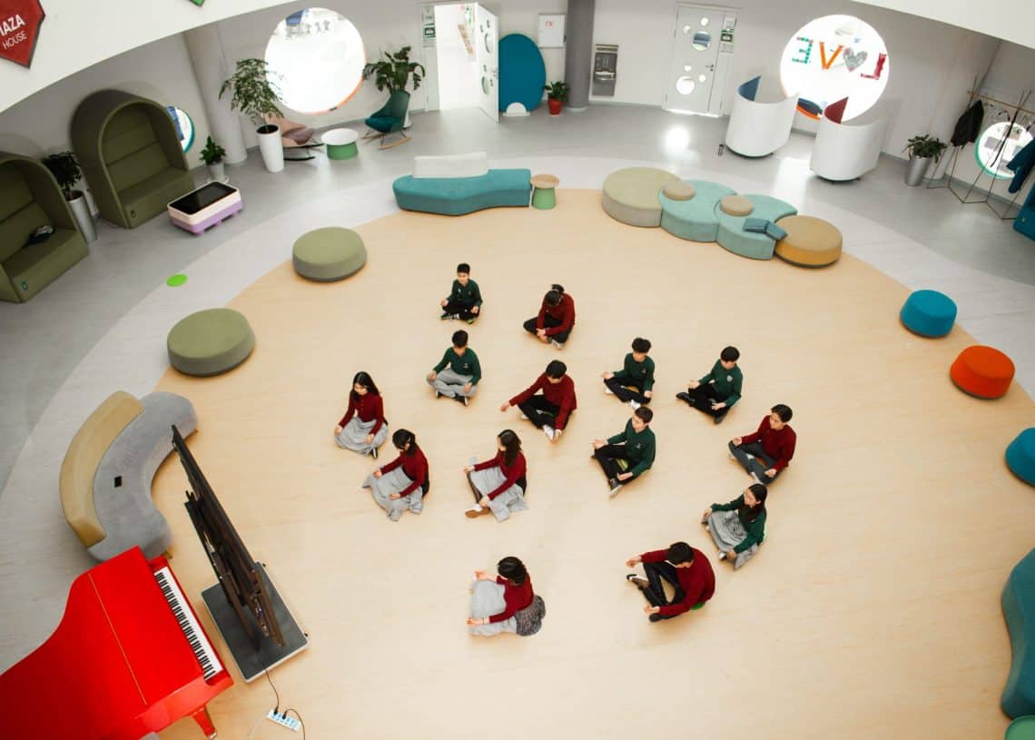 Дугуй суудал бүхий орчин үеийн өргөн уудам анги танхимын дээгүүр харагдана. Оюутнууд шалан дээр дэрэн дээр сууж, улаан төгөлдөр хуур дээр багшийн өөдөөс харан сууна. Загварлаг, муруй тавилга, гоёл чимэглэлийн элементүүд нь өрөөний эргэн тойронд тархсан бөгөөд энэ нь шинээр гарч ирж буй энтрепренерүүдэд урам зориг өгөх орчинг бүрдүүлдэг. Ургамал нь ногоон өнгө нэмдэг. - Business.MN